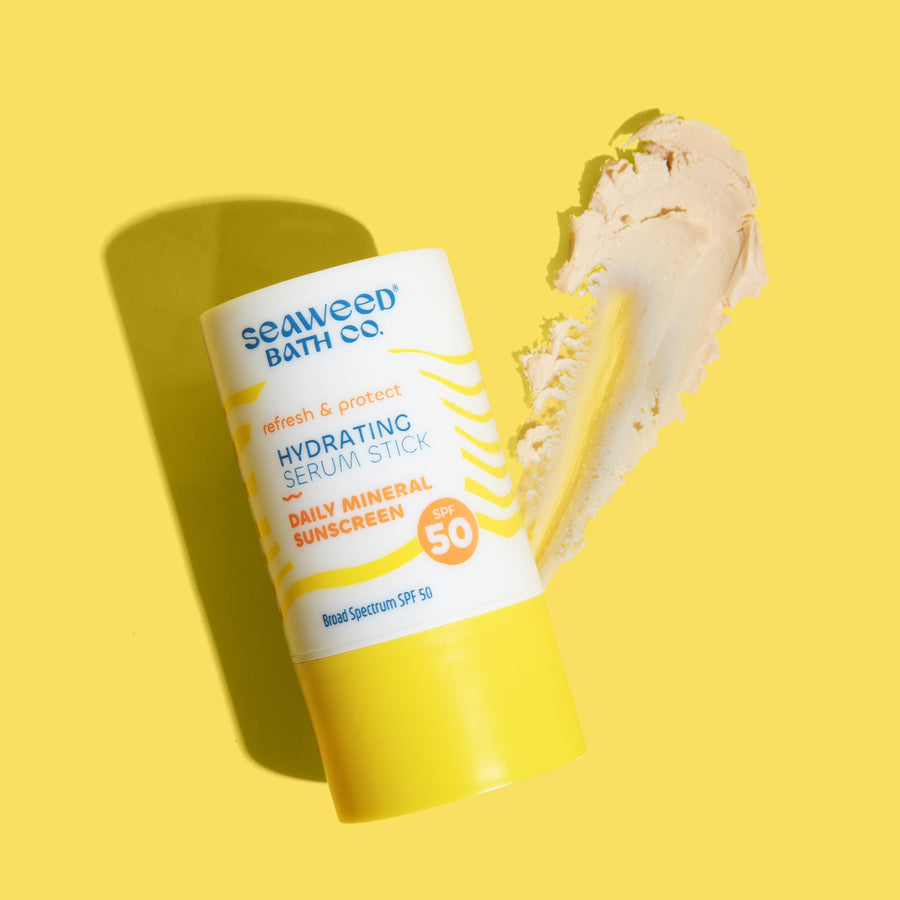 Seaweed Bath Co. Refresh & Protect Hydrating Serum Stick SPF 50 on yellow background with smear of creamy stick next to it.