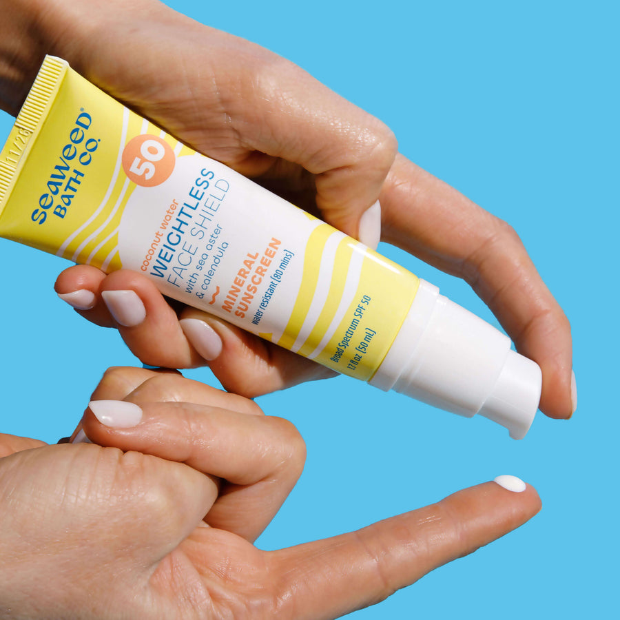 Hand pumping Weightless Face Shield SPF 50 onto finger of other hand.