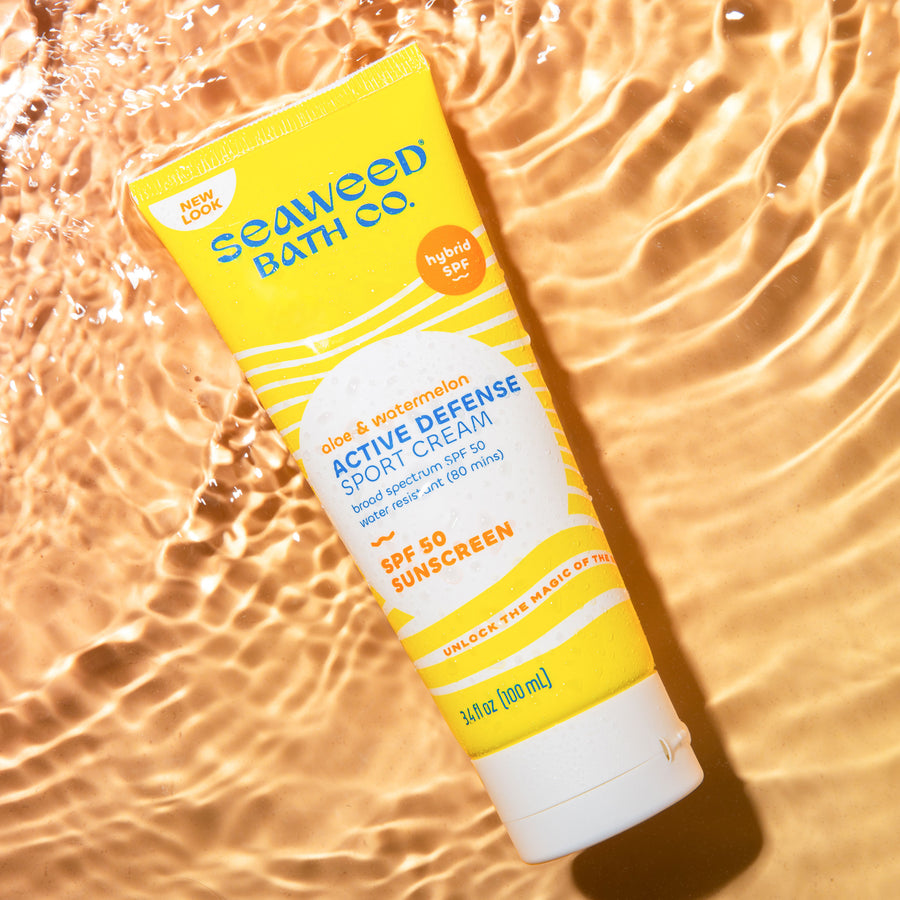 Active Defense Sport Cream SPF 50 Sunscreen tube laying in rippling water on sunset orange background.