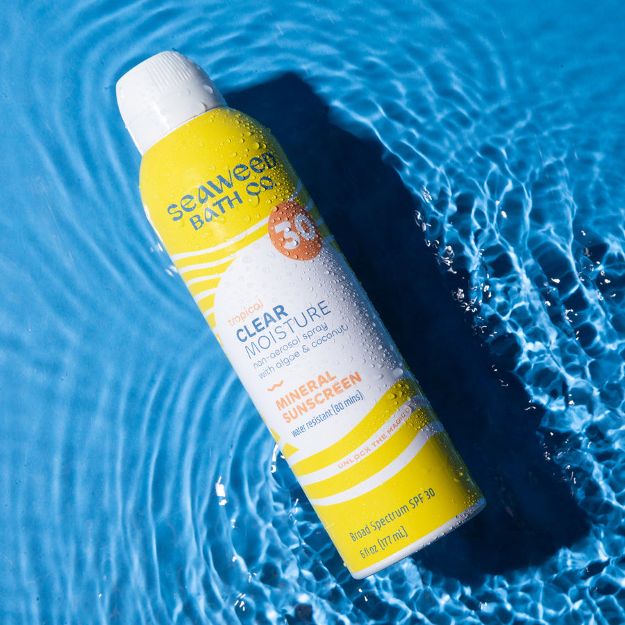Seaweed Bath Co. Clear Moisture Mineral Spray SPF 30 Sunscreen laying flat in rippling water on sky blue background.