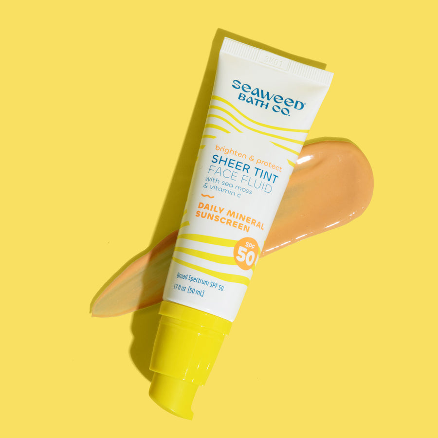 Seaweed Bath Co. Sheer Tint Face Fluid SPF 50 on yellow background laying on top of smear of tinted sunscreen product.