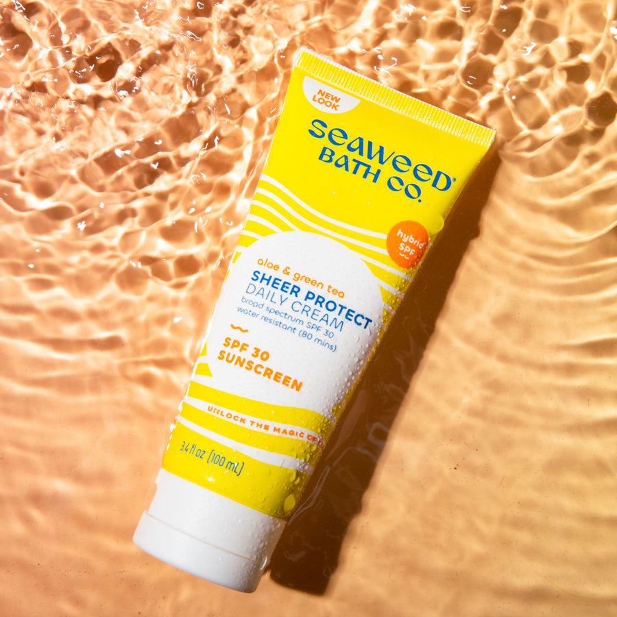 Sheer Protect Daily Cream SPF 30 Sunscreen tube laying in rippling water on sunset orange background. Seaweed Bath Co.