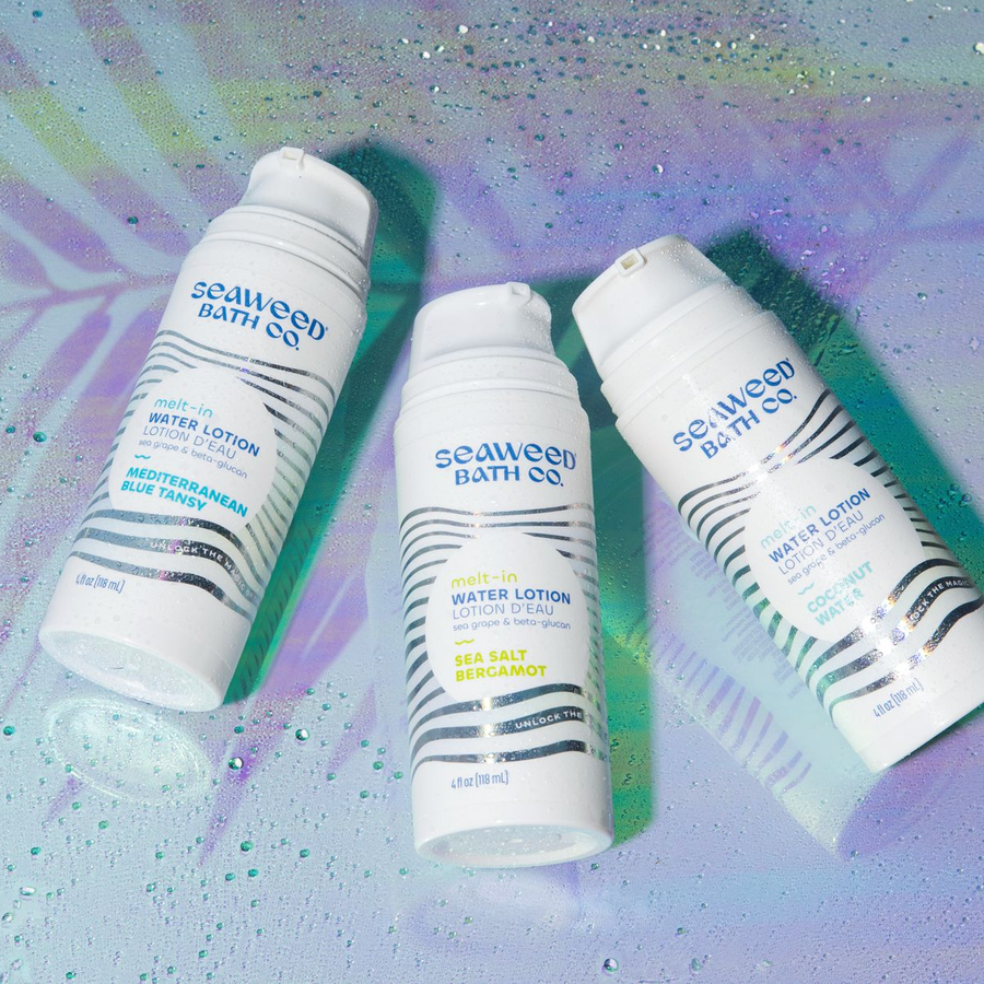 Seaweed Bath Co. Melt-In Water Lotion in all three ocean-inspired scents. Bottles laying on dewy, holographic background under a palm leaf shadow.